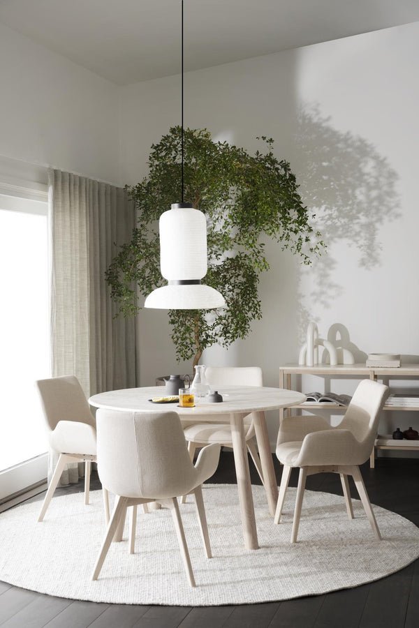 Minimalistisk matplats med runt vitt bord, beiga stolar och modern taklampa under gröna växter