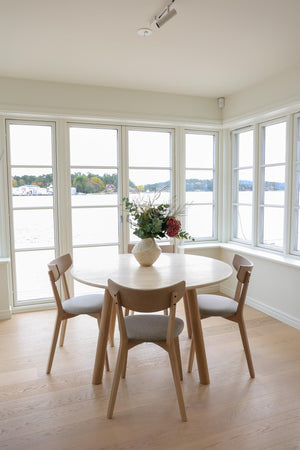 Runt matbord i ljust trä med fyra stolar vid fönster med sjöutsikt i skandinavisk stil