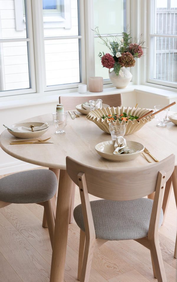 Runt matbord i ljust trä med stolar och elegant dukning i skandinavisk stil vid fönster