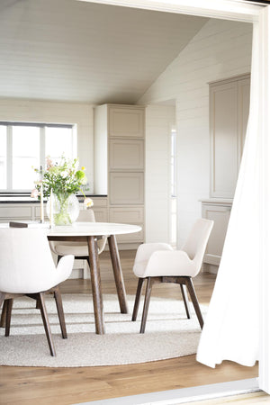 Ljus matplats med runt matbord, vita stolar med träben och beige skåp i skandinavisk stil