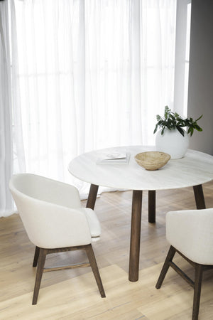 Runt matbord i vit marmor med träben och vita stolar i skandinavisk design vid fönster med vita gardiner