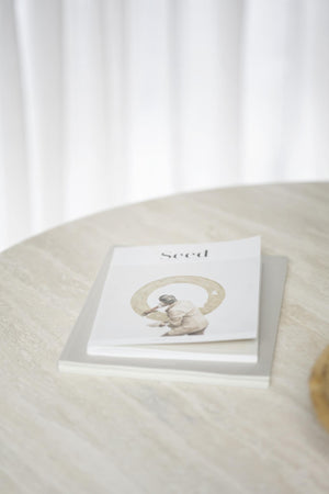 Konstbok med titeln "seed" ligger på marmorbord med neutrala färger och minimalistisk design