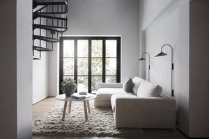 Minimalistiskt vardagsrum med beige soffa, spiraltrappa och svarta fönsterpartier med utsikt mot grönska