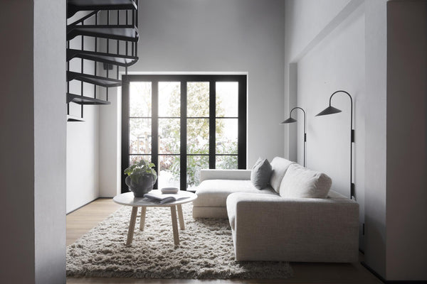 Minimalistiskt vardagsrum med beige soffa, spiraltrappa och svarta fönsterpartier med utsikt mot grönska