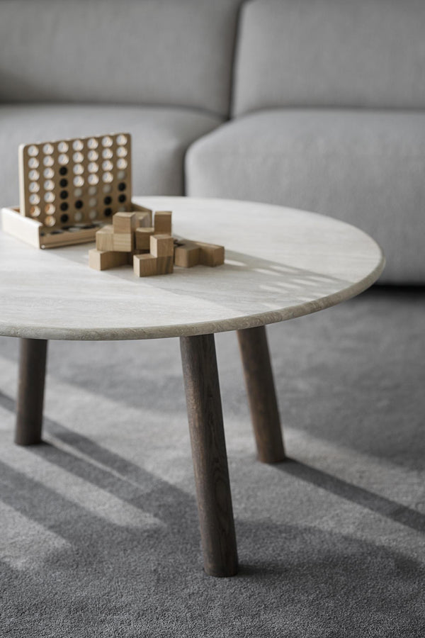 Runt soffbord i ljust trä med träpussel och brädspel, grå soffa i bakgrunden