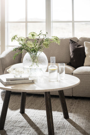 Runt soffbord i ljust trä med mörka ben, dekorerat med glasvas, böcker och karaffer i skandinavisk stil