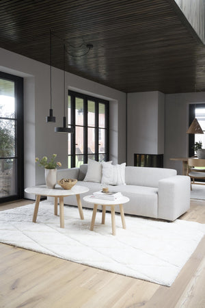 Minimalistiskt vardagsrum med grå soffa, svart ribbtak, vita soffbord och skandinavisk inredning