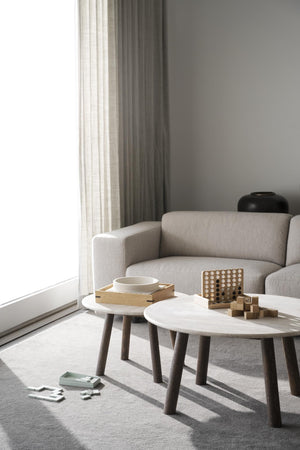 Minimalistiskt vardagsrum med grå soffa, runda soffbord i vit marmor och trä, naturligt ljus från fönster