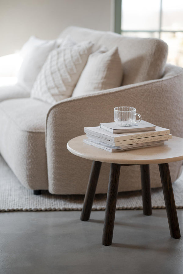 Runt soffbord i ljust trä med mörka ben, dekorerat med böcker och glasmugg bredvid beige soffa