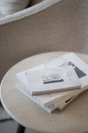 Glaskoppa med räfflad design på staplade tidningar på runt marmorbord i skandinavisk inredning