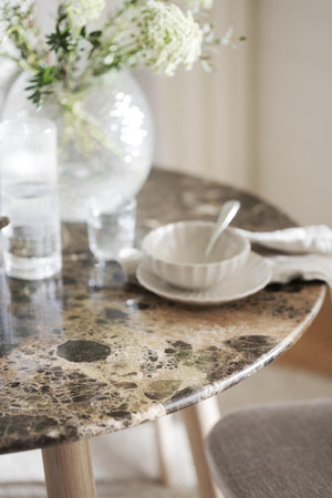 Runt marmorbord med snakeskin-mönster, vit tekopp och vas med blommor i ljus skandinavisk inredning