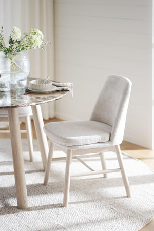 Ljus stoppad matstol i beige tyg vid runt matbord med marmortop och vit vas med blommor