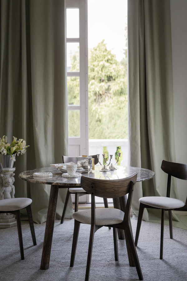 Matbord i marmor med träben och stolar i grå tyg, placerat framför fönster med gröna gardiner