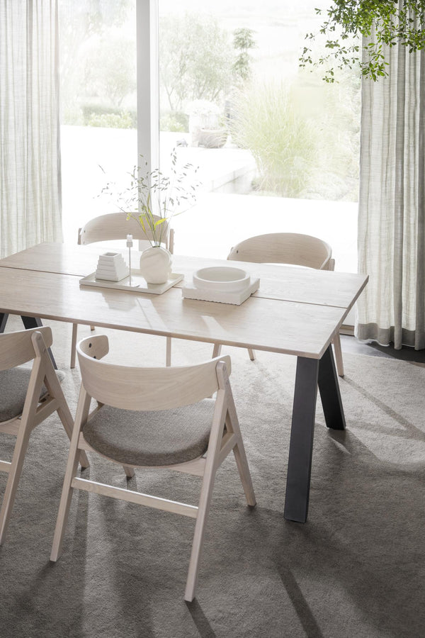 Ljus matplats med ljust träbord, stolar i vitpigmenterad ek och vita gardiner mot stora fönster