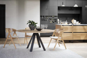 Runt matbord i ljust trä med svarta ben omgivet av tre matchande stolar i modern skandinavisk design