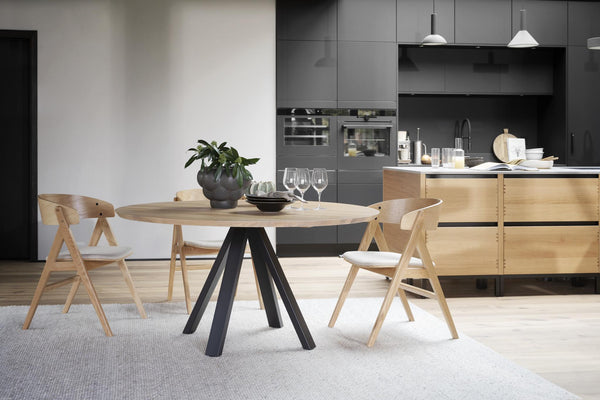 Runt matbord i ljust trä med svarta ben omgivet av tre matchande stolar i modern skandinavisk design