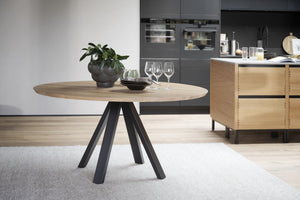 Runt matbord med ekfanér och svarta ben i modern skandinavisk stil, placerat i öppet kök