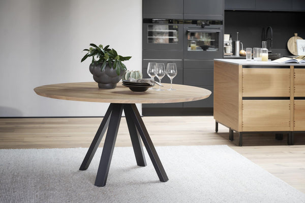 Runt matbord med ekfanér och svarta ben i modern skandinavisk stil, placerat i öppet kök
