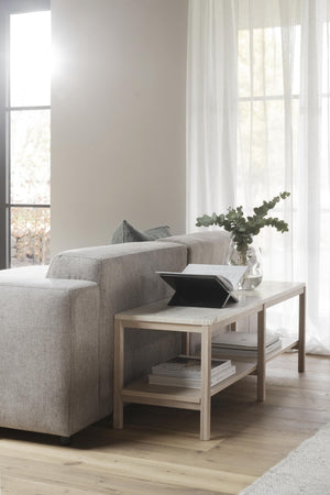 Ljust vardagsrum med beige soffa, soffbord i trä med böcker och vas med eukalyptus vid fönster