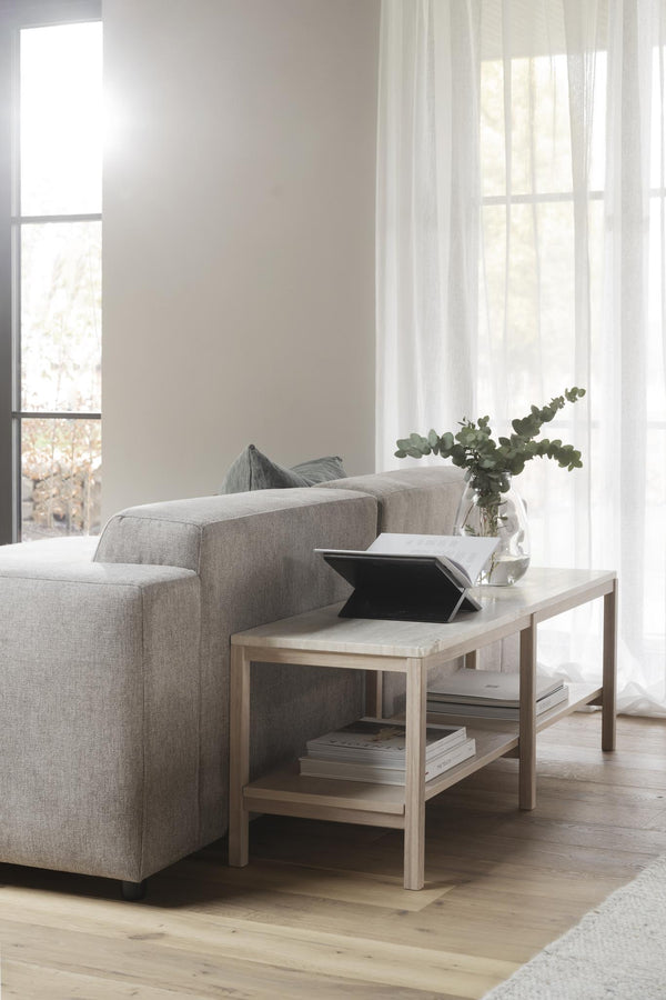 Ljust vardagsrum med beige soffa, soffbord i trä med böcker och vas med eukalyptus vid fönster