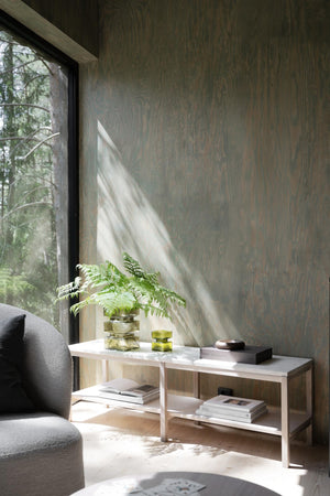 Ljust vardagsrum med ljust träsoffbord, grön växt, böcker och utsikt mot skog genom stort fönster