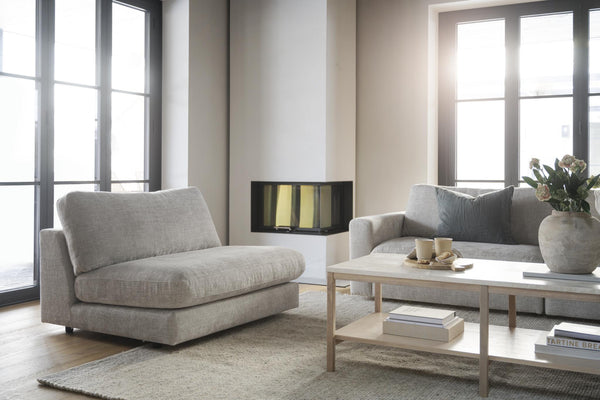 Grå soffa och fåtölj i modernt vardagsrum med ljusa träbord och öppen spis