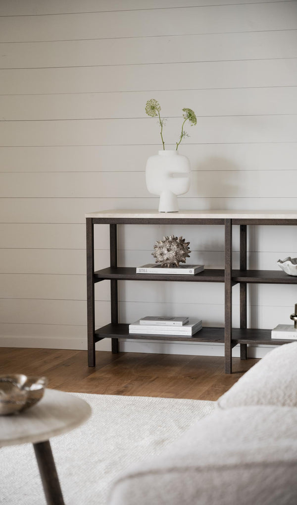 Mörkt träskåp med öppna hyllor, dekorerat med vit vas, böcker och snäcka i minimalistiskt vardagsrum