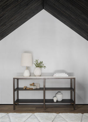 Konsolbord i mörkt trä med hyllplan, dekorerat med lampa, vas och böcker mot vit vägg