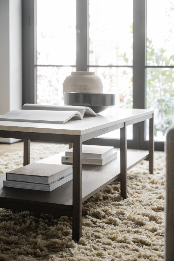 Soffbord i vit marmor och metall med böcker på fluffig beige matta framför fönster