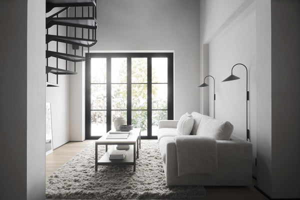 Minimalistiskt vardagsrum med grå soffa, spiral trappa, svarta stålramar och fluffig matta i vitt