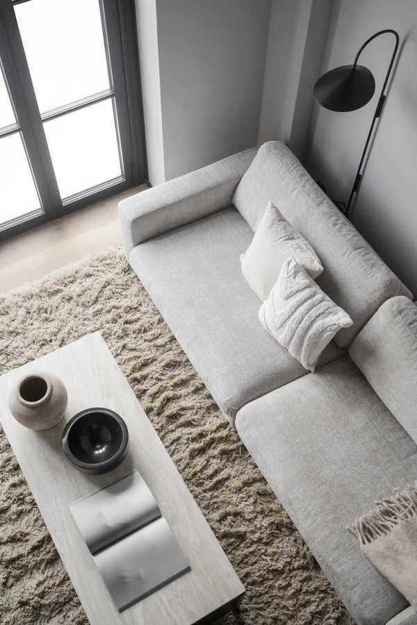 Minimalistiskt vardagsrum med grå soffa, vit soffbord, beige fluffmatta och svart golvlampa vid fönster