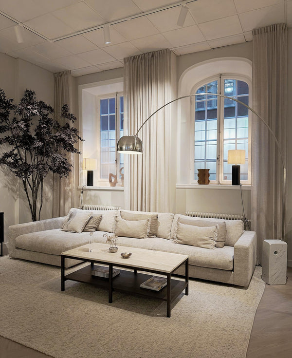 Beige modulsoffa med schäslong i ljust vardagsrum med högt i tak och stora fönster med bågar