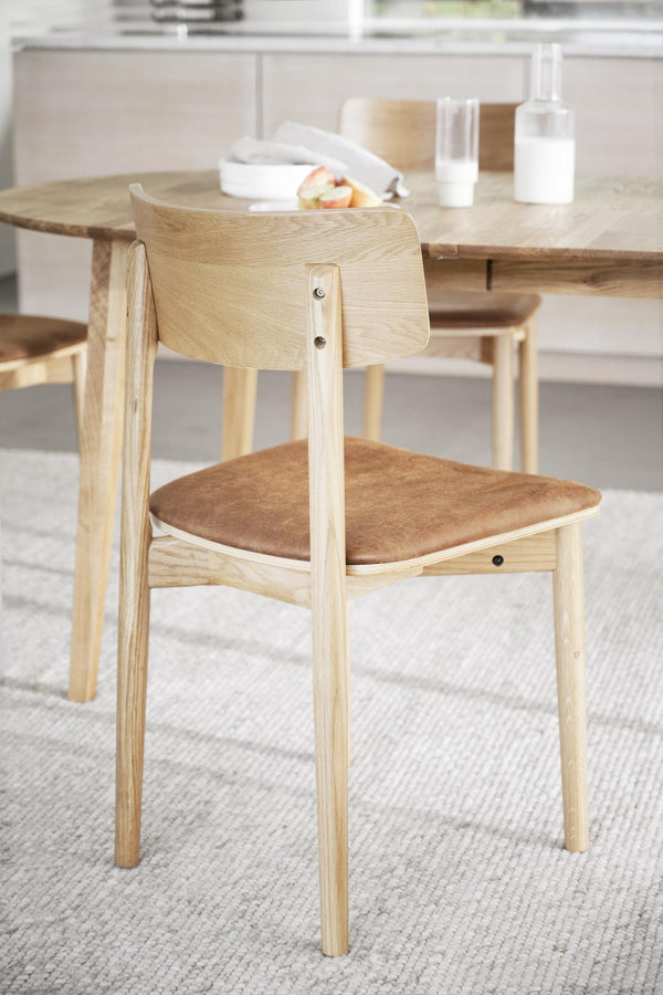 Ljus ekfanerad stol med stoppad brun sits och böjd rygg vid matbord i skandinavisk stil