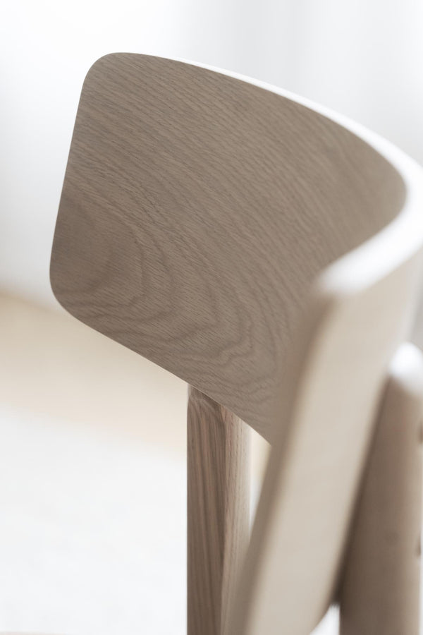 Närbild på ryggstöd och ben i ljust trä på en minimalistisk stol med naturlig trästruktur