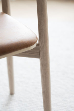 Närbild på ljust trämöbel med rundad sits och slanka ben i minimalistisk skandinavisk design