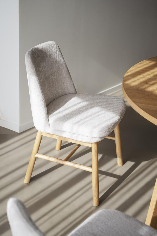 Grå stoppad stol med träben i ljust trä bredvid runt träbord i minimalistisk skandinavisk stil