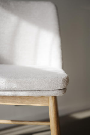 Närbild på ljusgrå stoppad sittdyna på stol med träben i ljust trä, minimalistisk skandinavisk design