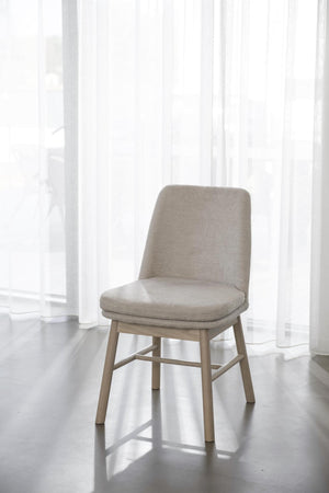 Beige stoppad stol med ljusa träben i modernt rum med vita genomskinliga gardiner