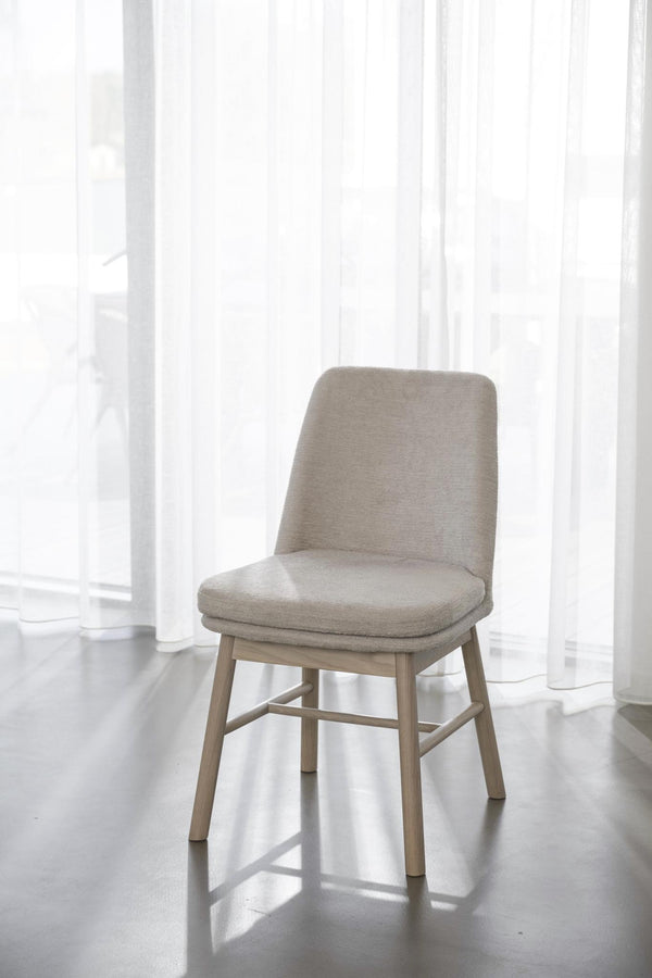 Beige stoppad stol med ljusa träben i modernt rum med vita genomskinliga gardiner