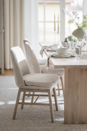 Ljus matplats med beige stoppade stolar vid träbord, uppdukat med vita porslin och vinglas i skandinavisk stil