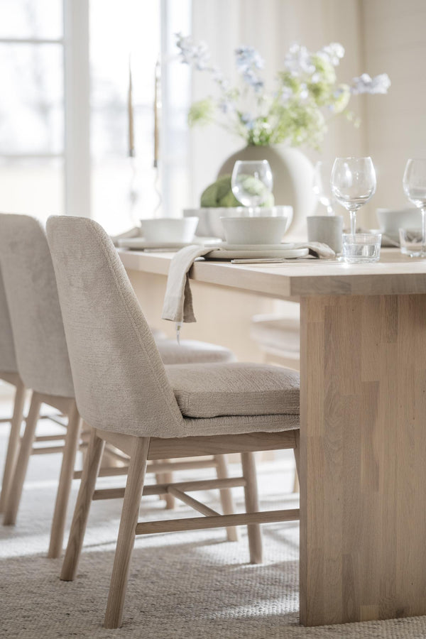 Ljus matgrupp i trä med beige stoppade stolar, uppdukat med glas och vit porslin i skandinavisk stil