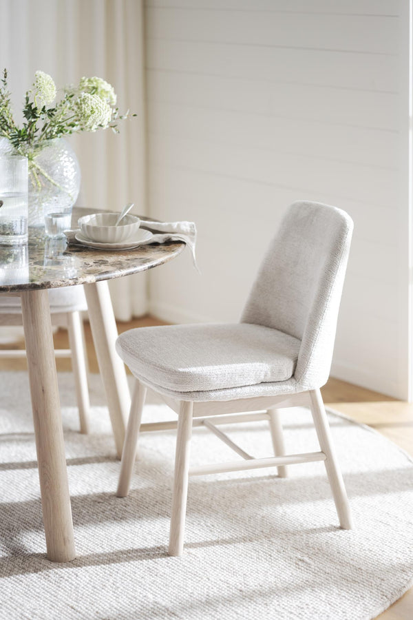 Beige stoppad stol vid runt marmorbord med vita blommor i ljust skandinaviskt matrum