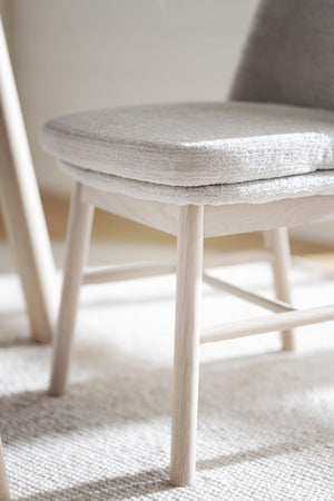 Grå stolsdyna i mjukt tyg på ljus trässtol med rundad sits och spjälor