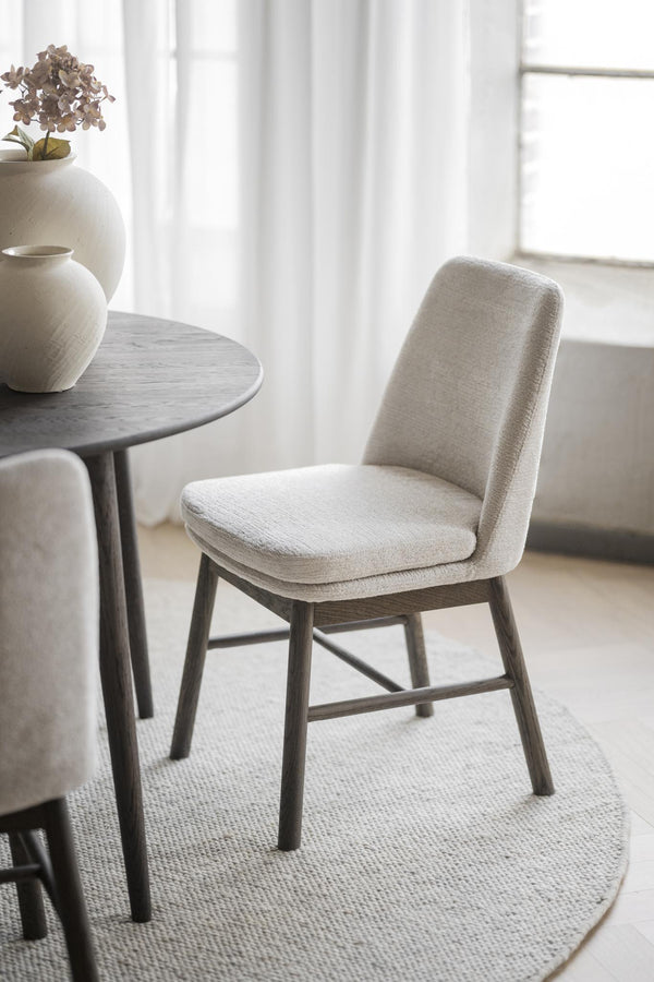 Beige stoppad matstol med mörkgrå träben vid runt matbord i skandinavisk stil