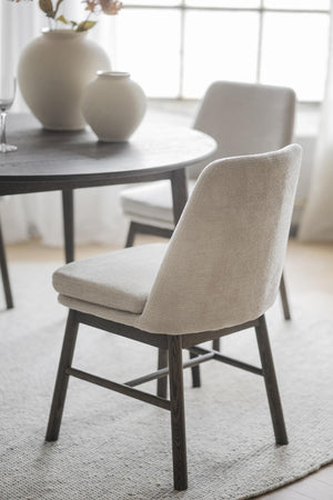 Beige matstol med mörka träben vid runt matbord med vita vaser i minimalistisk matsal