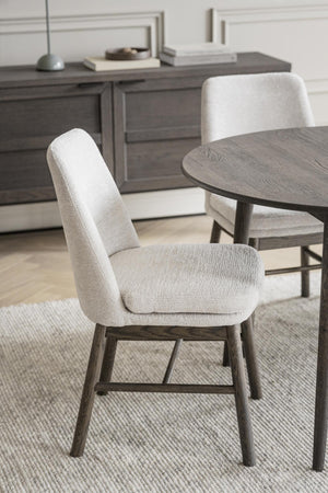 Stoppad matstol med beige klädsel och mörkgrå träben vid runt matbord i modern skandinavisk stil