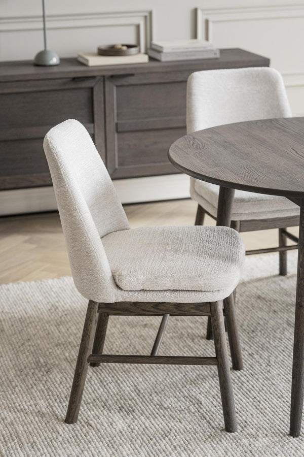 Stoppad matstol med beige klädsel och mörkgrå träben vid runt matbord i modern skandinavisk stil