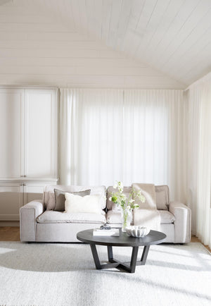 Ljust vardagsrum med beige soffa, svart runt soffbord och vita gardiner i minimalistisk skandinavisk stil