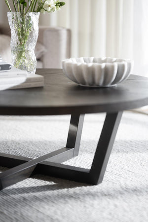 Soffbord med rund grå träskiva och svarta metallben, dekorerat med vit skål och glasvas med blommor