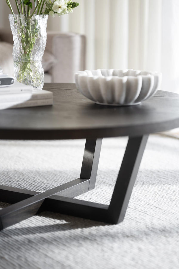 Soffbord med rund grå träskiva och svarta metallben, dekorerat med vit skål och glasvas med blommor